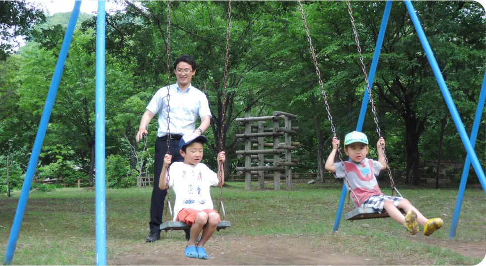 公園でブランコに乗る2人の子供を後ろから押している藤原たかし氏