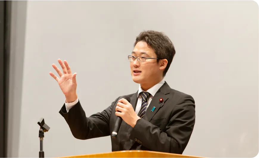 藤原たかし氏が演説中にマイクを持ちながら手を上げて話している様子